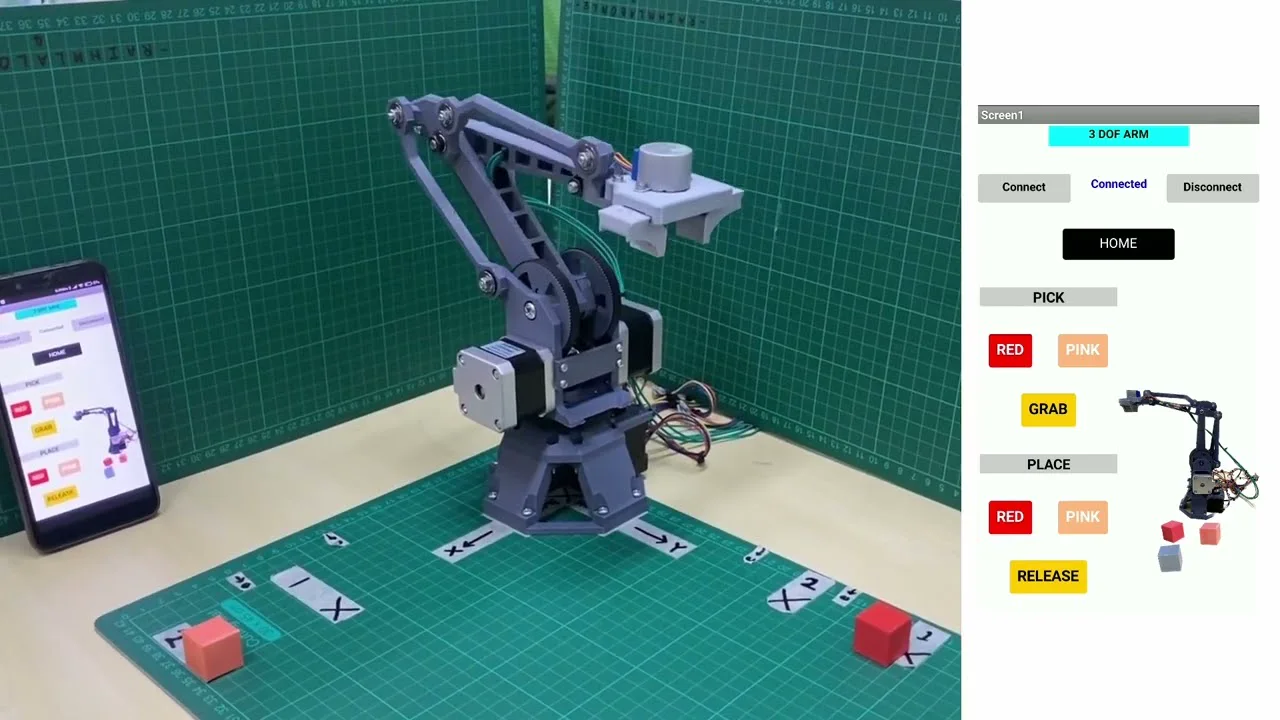 The three-jointed robot arm on a cutting mat beside a phone running its control app
