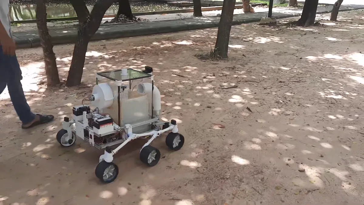 The rover driving along a shaded path under trees, with leaf litter on the ground