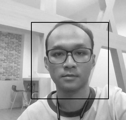A grayscale webcam photo with a square detection box drawn around the subject's face